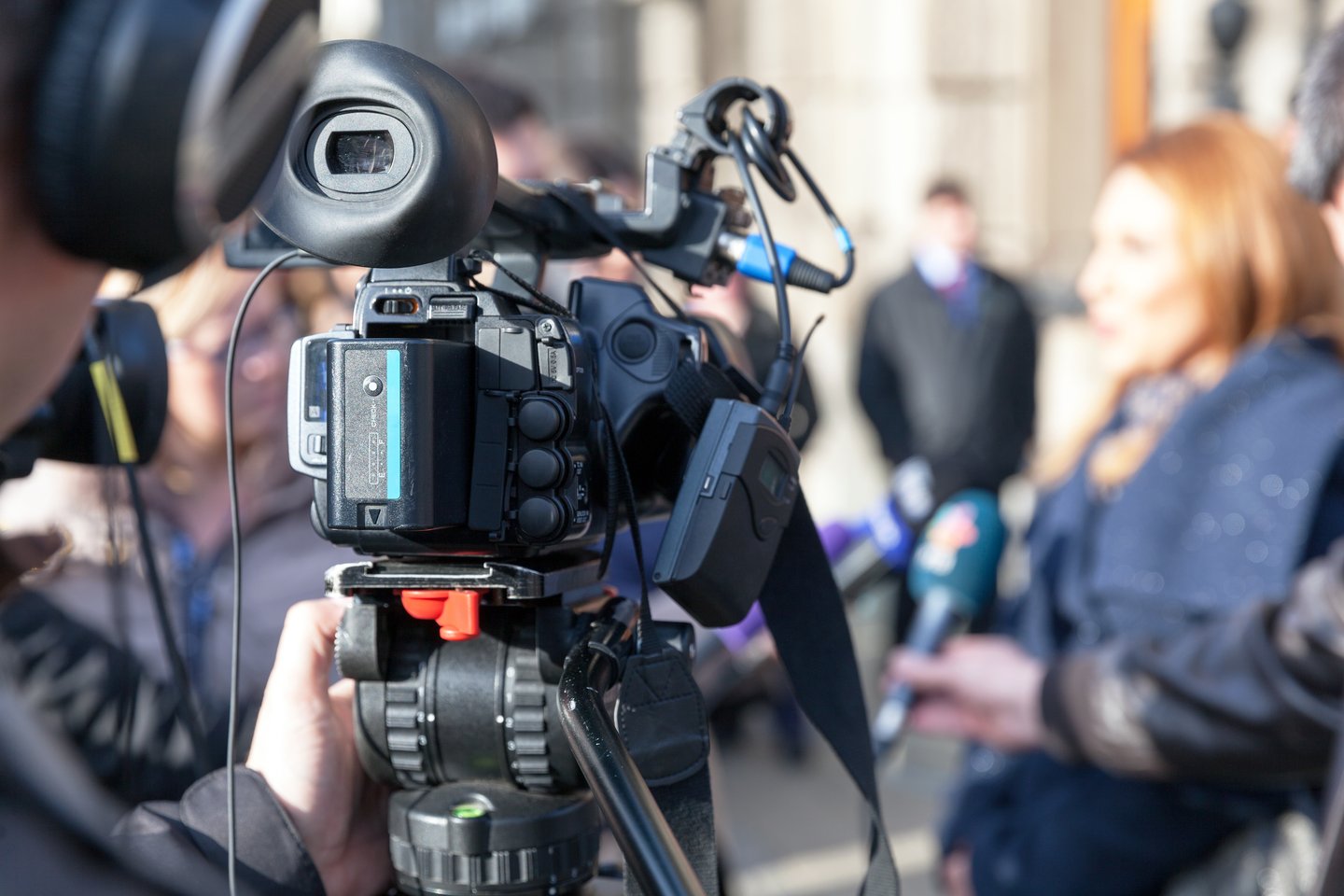 TV camera in foreground while woman speaks in background